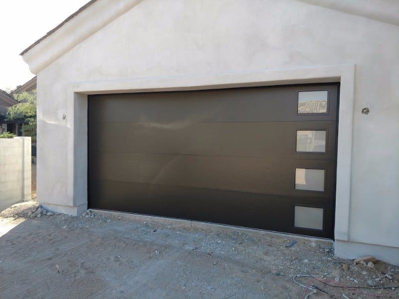 Dark bronze modern garage door with offset windows on a white stucco home