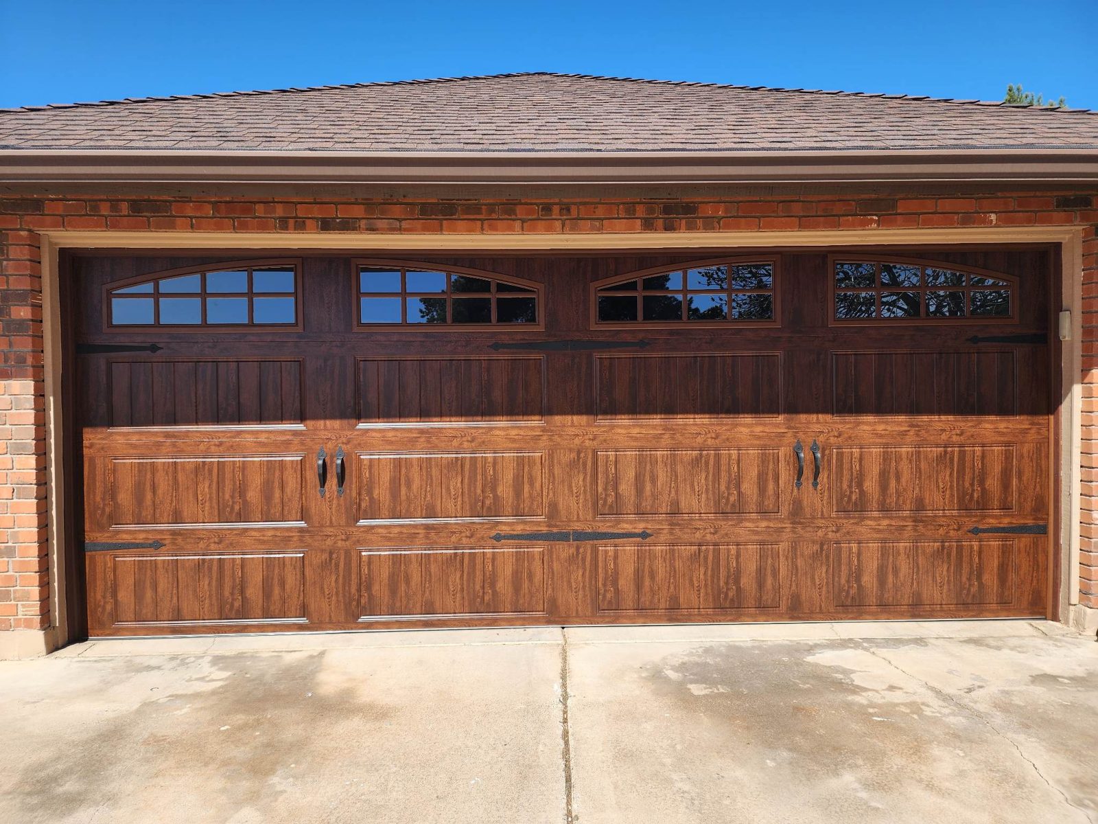 Wood grain carriage house garage door with arched windows on a brick home