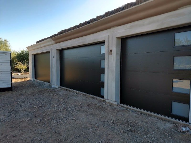 Three black modern garage doors with offset windows on a new build home
