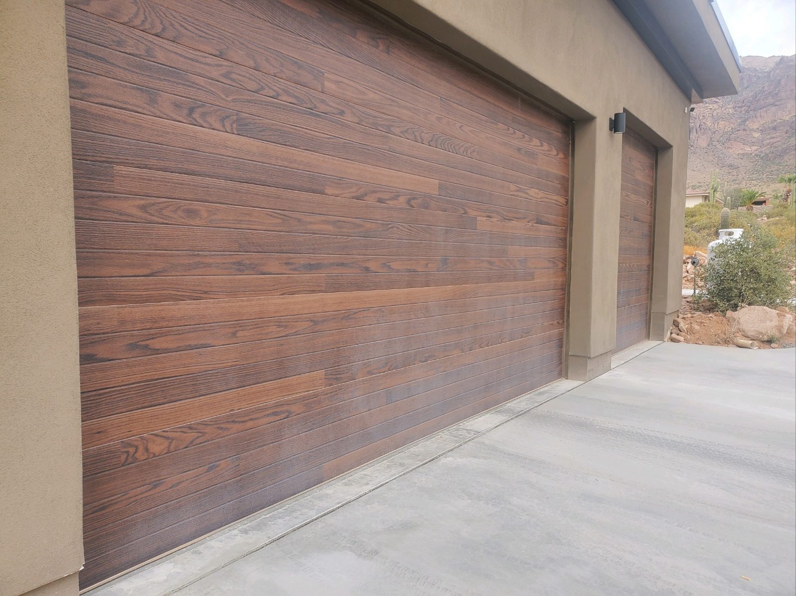 Walnut plank double and single garage doors on a desert home with mountains behind